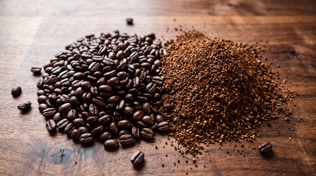 Overhead view of whole roasted coffee beans beside freshly ground coffee on a wooden counter