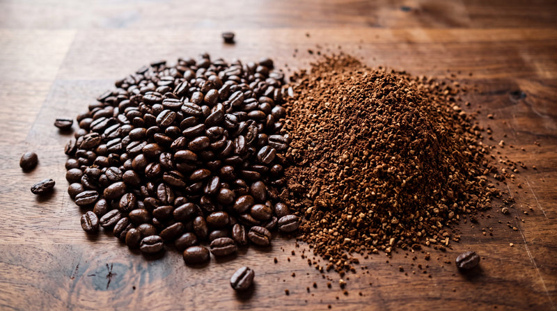 Overhead view of whole roasted coffee beans beside freshly ground coffee on a wooden counter