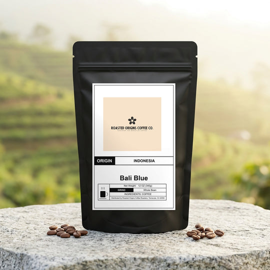 Bali Blue coffee bag standing on pale granite outdoors, roasted beans scattered around its base