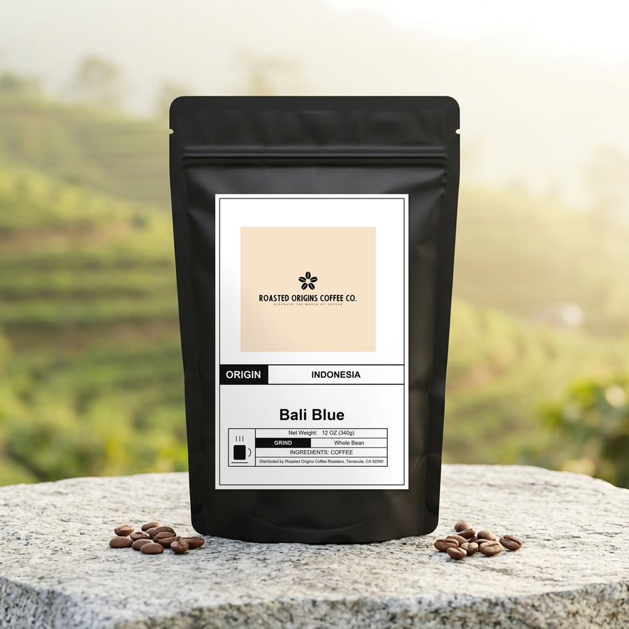 Bali Blue coffee bag standing on pale granite outdoors, roasted beans scattered around its base
